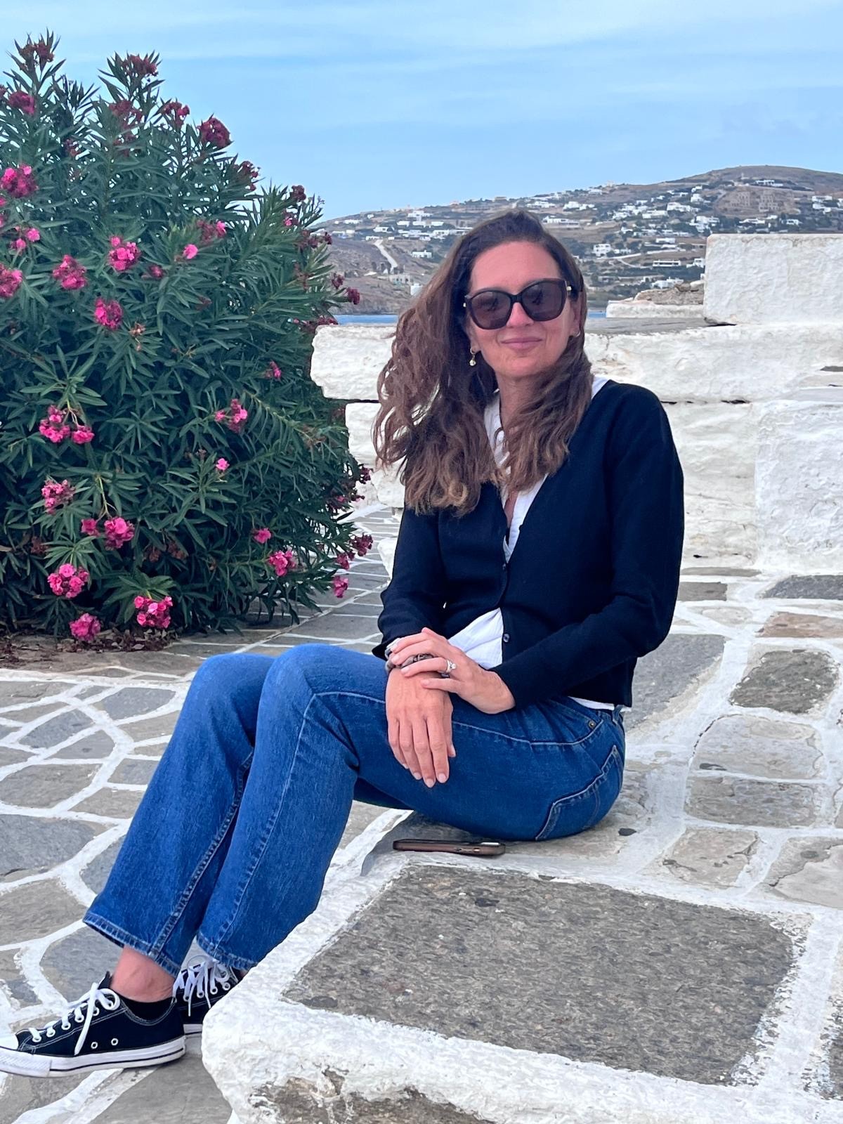 Majo, smiling, sitting on a whitewashed stone step by the sea next to a flowering bush